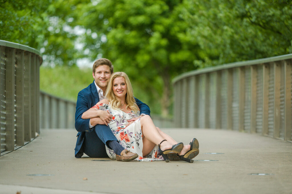 Taylor and Michael pose during their Nashville wedding engagement photo shoot sitting down on a bridge together.