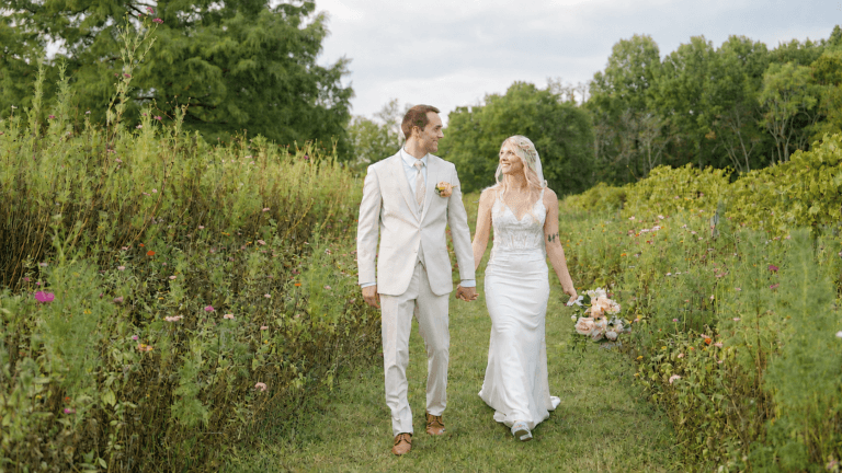 A happy bride and groom hold hands and walk through the flower gardens with their Nashville wedding photographer.