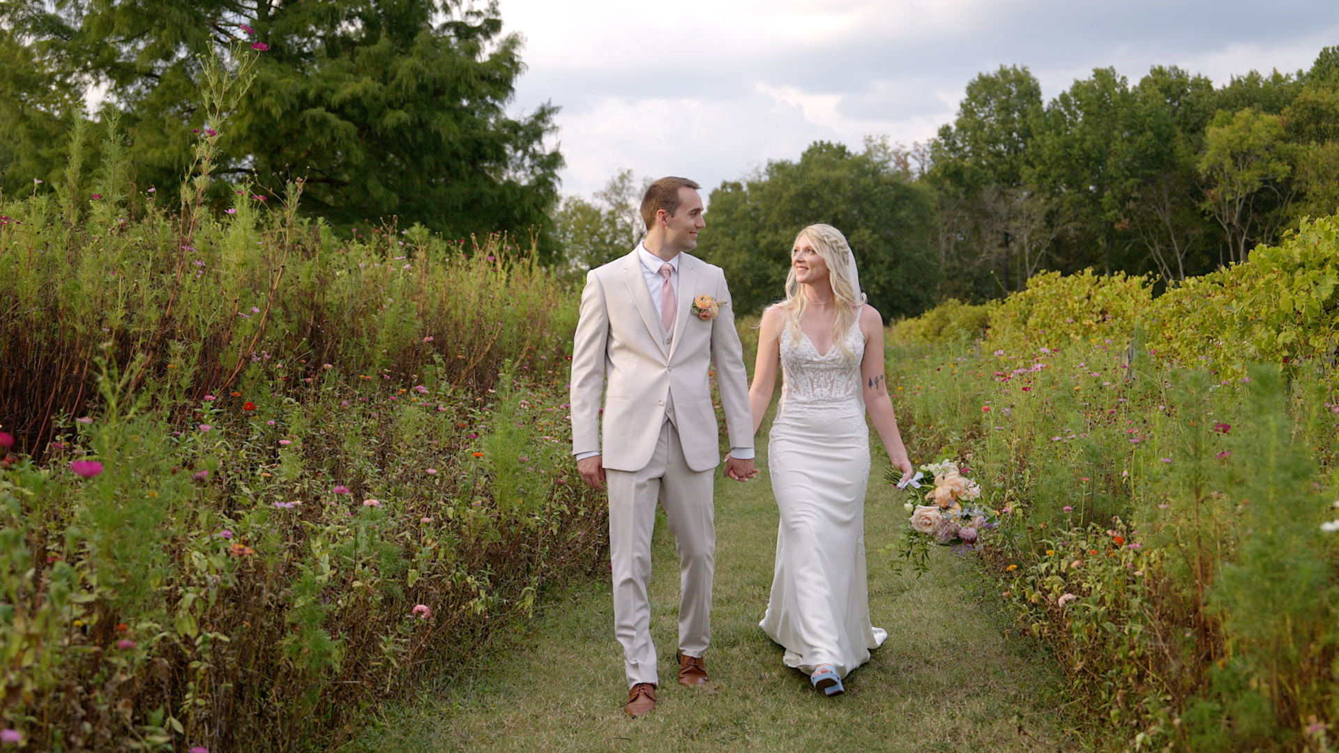 A happy bride and groom hold hands and walk through the flower gardens with their Nashville wedding photographer.