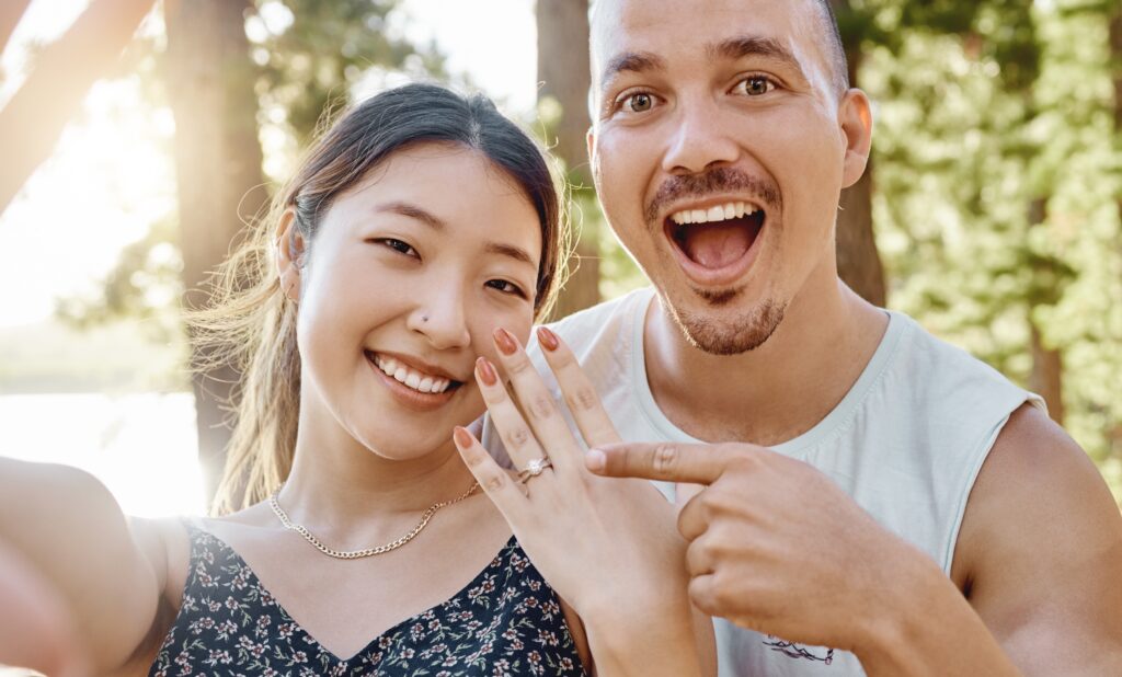 Engaged couple wedding planning in Nashville smiling with groom pointing to his fiancee's engagement ring, outside at Radnor Lake.