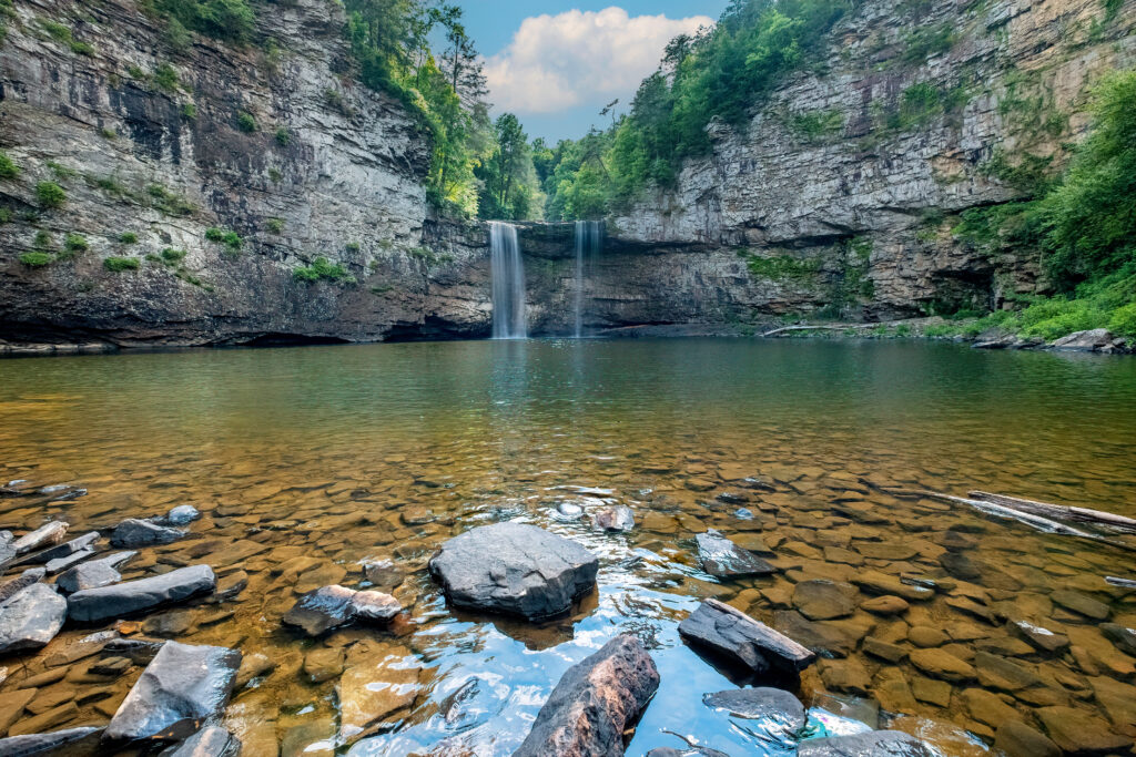 Scenic view of Cane Creek Falls at Fall Creek Falls State Park in Tennessee, featuring a cascading waterfall into a clear, rocky pool surrounded by dramatic cliffs and lush greenery — a breathtaking outdoor wedding location for nature-loving couples.