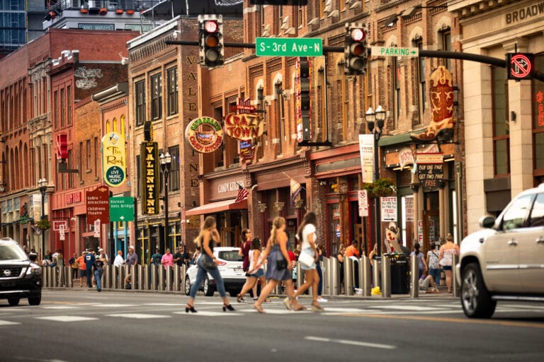 Group of women crossing Broadway in downtown Nashville during a bachelorette weekend, with iconic honky-tonks, bars, and neon signs in the background—perfect for girls’ trips and bride-to-be celebrations.