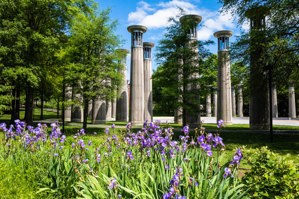 Springtime view of the Carillon pillars at Bicentennial Capitol Mall State Park in Nashville, Tennessee, with blooming purple irises and lush greenery — a unique outdoor setting for elegant wedding photography and skyline-inspired wedding videography.
