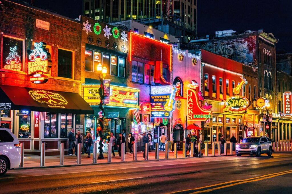 Broadway Street in downtown Nashville lit up with neon bar signs at night, a lively backdrop for bachelorette parties and girls’ weekend celebrations.