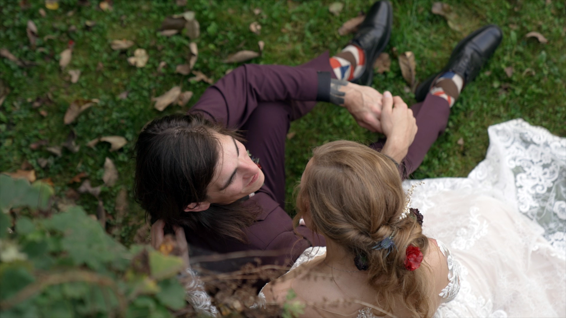 Overhead view of bride and groom sharing a quiet moment on the grass at their fall wedding at Ruskin Cave in Dickson, TN. Filmed by With This Ring, Nashville wedding videographers, highlighting the bride’s lace dress and floral hair accessory.